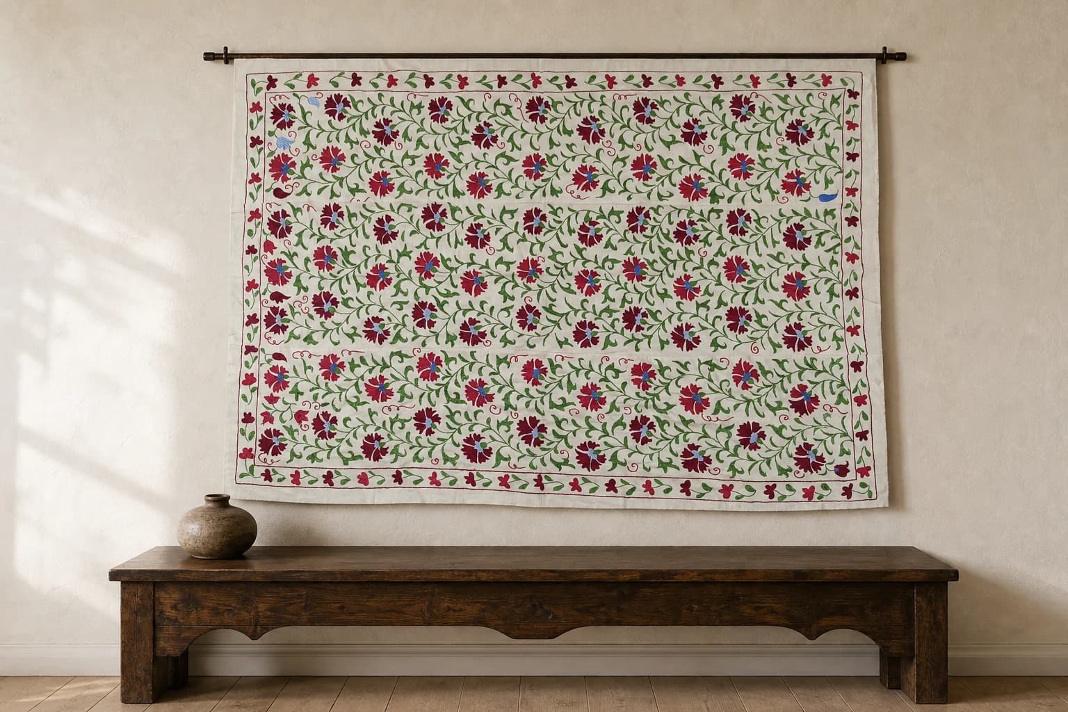 Large embroidered Suzani with red flowers and green vines on an ivory ground.